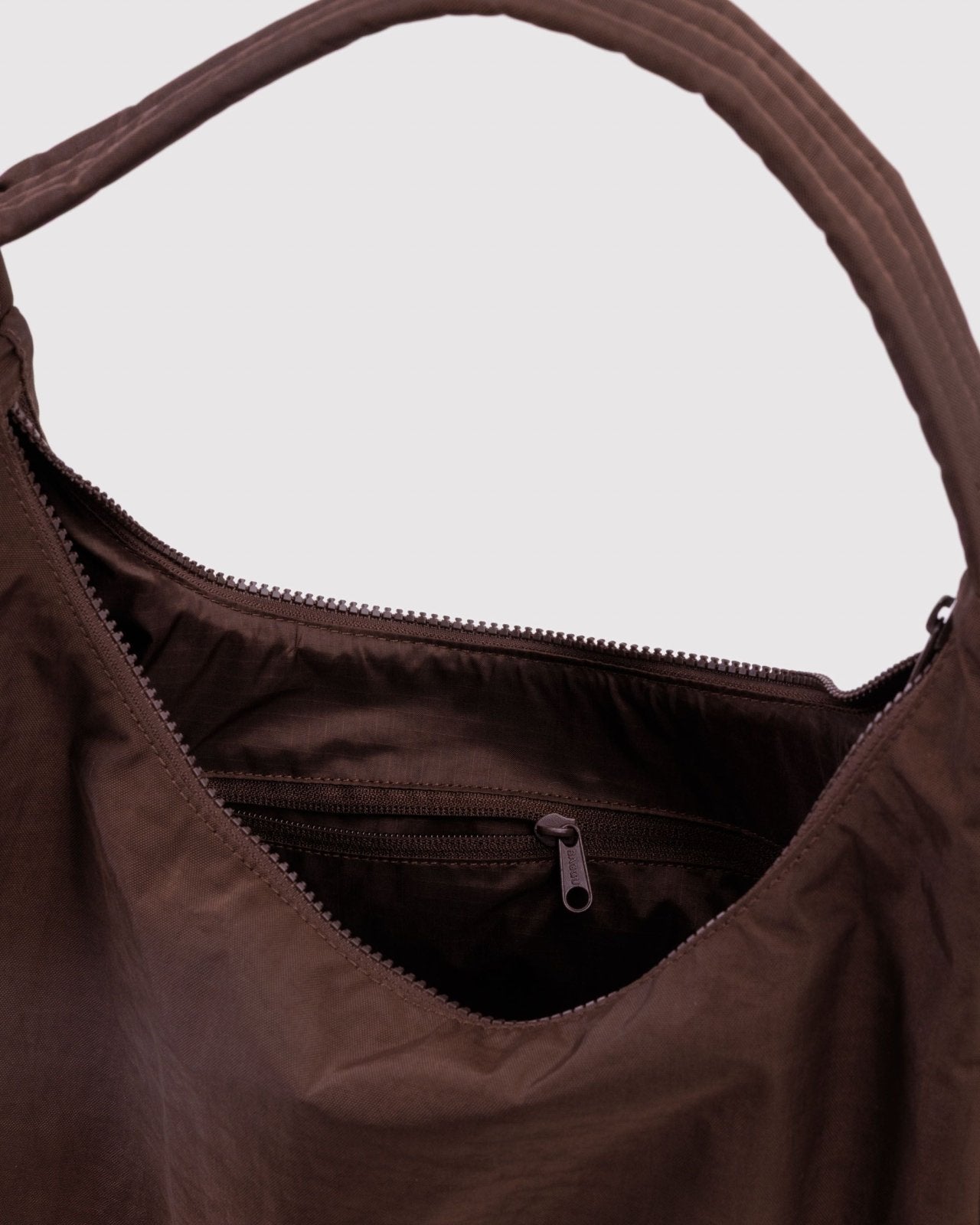 Schultertasche aus Nylon in Kaffeebraun von BAGGU, am Körper getragen